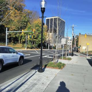 A sunny day on a city street featuring traffic signals and a mixture of urban buildings and greenery.