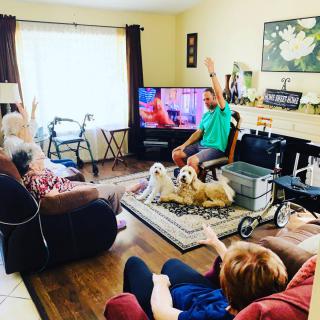 A group of people and two dogs relaxing in a living room with a television on.
