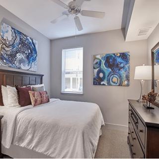 A cozy bedroom featuring colorful artwork, a neatly made bed with pillows, and elegant decor.