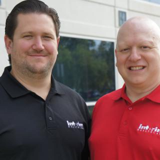 Two men smiling outdoors, wearing polo shirts.