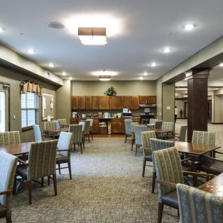 A spacious dining area with multiple tables and chairs, featuring warm lighting and an open kitchen setup.