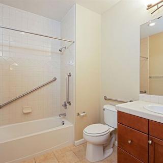 A clean and modern bathroom featuring a bathtub with grab bars, a toilet, and a sink with a mirror.