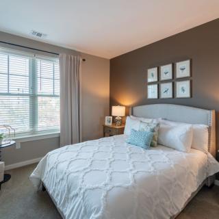 A cozy bedroom with a large window, neatly made bed, and elegant decor.