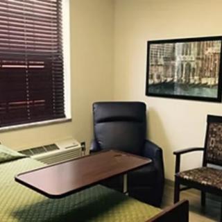 A small room with a bed, a reclining chair, and a table near the window.