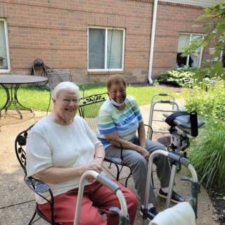 Two elderly individuals sitting outside with walkers, enjoying a sunny day.