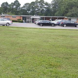 A view of a building with a parking lot, surrounded by well-maintained grass and trees.