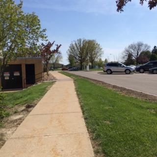 A sidewalk next to a parking lot with cars and trees on a sunny day.