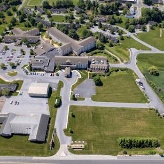 An aerial view of a complex featuring multiple buildings, parking facilities, and surrounding green spaces.