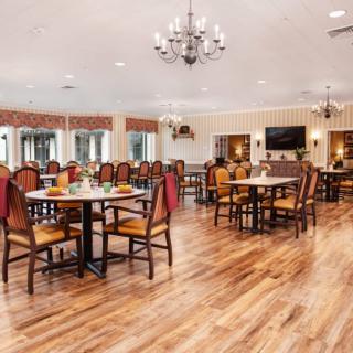 A spacious dining area with elegant chandeliers and neatly arranged tables and chairs on a hardwood floor.