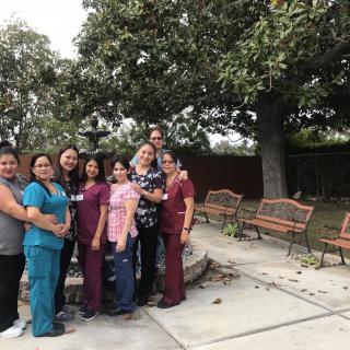 A group of people standing together in a garden setting with benches and trees in the background.