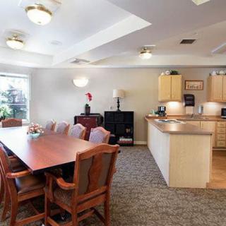A spacious dining and kitchen area with a large wooden table, chairs, and bright ceiling lights.