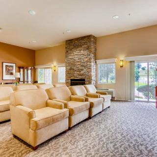 A cozy living room with a row of comfortable armchairs facing a stone fireplace, complemented by large windows and warm lighting.
