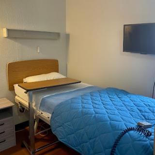 A clean and minimalistic hospital patient room featuring a bed with a blue blanket and a television.