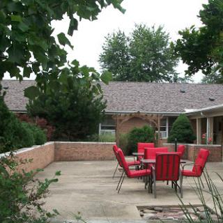 A cozy outdoor patio area featuring a set of red chairs and a table, surrounded by greenery.