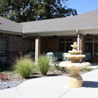 A serene courtyard featuring a decorative fountain surrounded by lush greenery and a brick building.