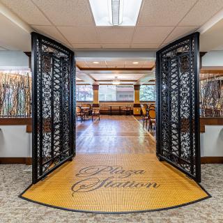 An inviting restaurant entrance with decorative iron gates leading to a spacious dining area with wooden floors.