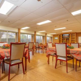 A spacious dining room with neatly arranged tables and chairs, featuring warm lighting and wood flooring.