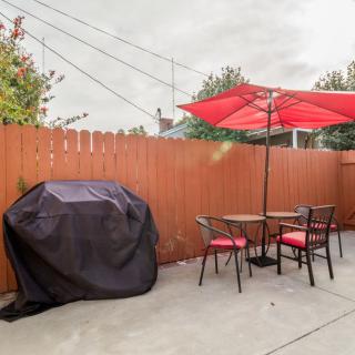 A cozy patio with a table and chairs under a red umbrella, next to a covered grill.