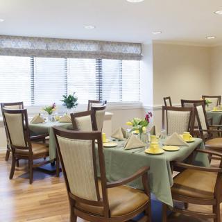 A well-lit dining room with neatly arranged tables and chairs, adorned with flowers and set for a meal.