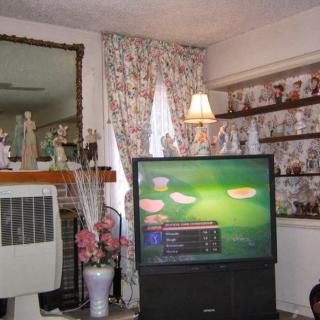 A cozy living room featuring an old television, floral curtains, and decorative shelves.