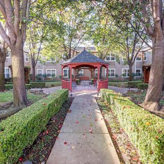A peaceful garden pathway leading to a red gazebo surrounded by lush greenery in a residential area.