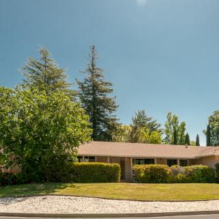 A suburban house surrounded by trees and a well-maintained front yard on a sunny day.