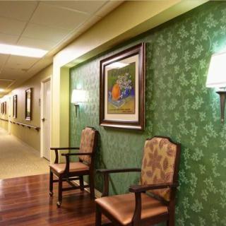 A hallway with chairs and artwork on green wallpapered walls, illuminated by wall lamps.