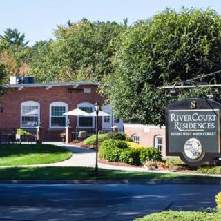 A brick building with a sign reading 'River Court Residences' surrounded by greenery and trees.
