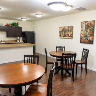A cozy dining area with wooden tables and chairs, adjacent to a small kitchen space.