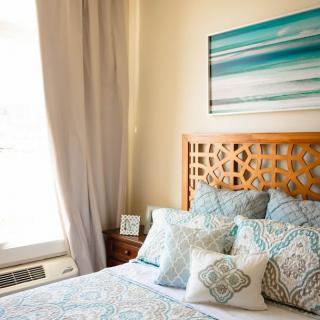 A cozy bedroom with patterned pillows and artwork on the wall.