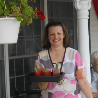 A woman smiling while carrying a tray of drinks on a porch.