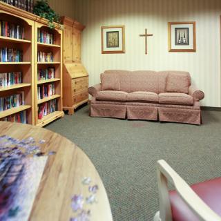 A cozy living room with a sofa, bookshelves, and religious decor.