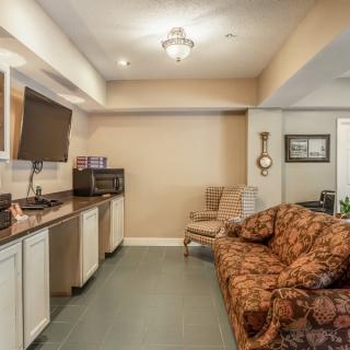 A cozy living space featuring a kitchenette with a microwave, a television mounted above, and comfortable seating including a patterned sofa.