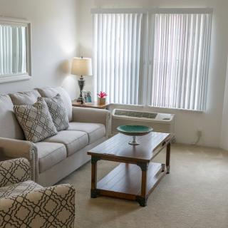 A cozy living room with a sofa, armchair, and coffee table near a window with blinds.