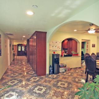 A spacious hallway with decorative tile flooring leads to a kitchen and dining area, featuring wooden cabinets and an archway.
