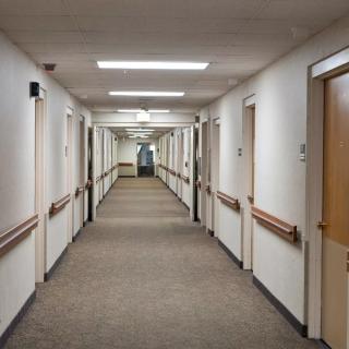 A long indoor corridor with doors on either side and bright overhead lighting.