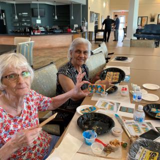 Two elderly women engage in a painting activity at a community center.