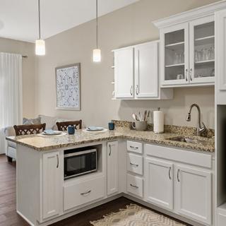 A modern kitchen with white cabinets and granite countertops, featuring pendant lighting and stainless steel appliances.