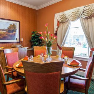 A cozy dining room with a round table set for four, featuring elegant window curtains and floral centerpiece.