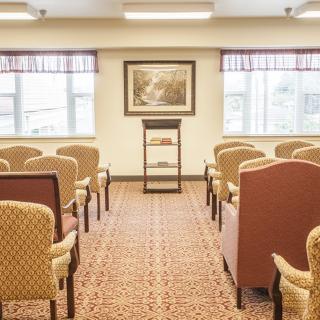 An empty lecture room with rows of chairs, a podium, and windows letting in natural light.