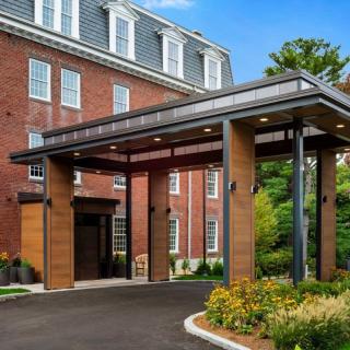 The entrance of a brick building with a modern canopy and neatly landscaped surroundings.