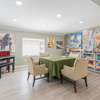 A modern dining area featuring an artfully decorated wall, a table with a green tablecloth, and beige chairs.