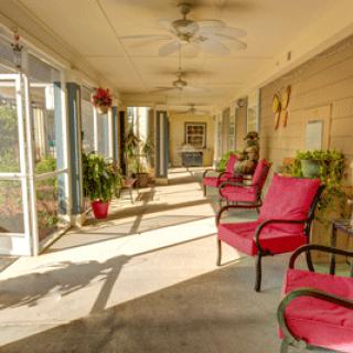 A sunlit porch with red-cushioned chairs and various potted plants.