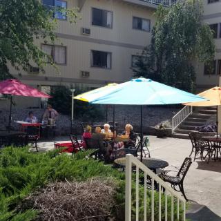 A sunny day on a patio with colorful umbrellas and seating in front of an apartment building.