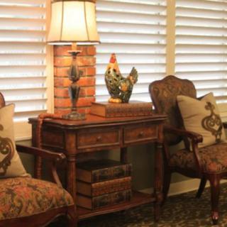 A cozy interior setup with vintage furniture, including a wooden table and chairs, a decorative rooster figure, and a lamp.