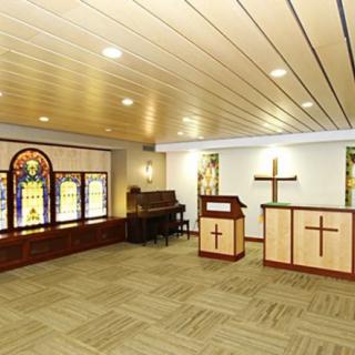 A serene chapel interior featuring stained glass windows, a piano, and an altar adorned with a cross.