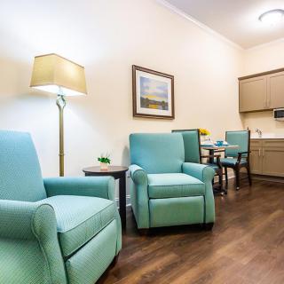 A cozy living room with teal armchairs, a floor lamp, and a small dining area in the corner.