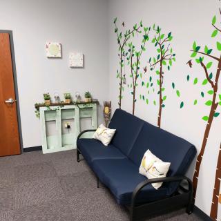A cozy waiting room with a blue couch and tree-themed wall art.