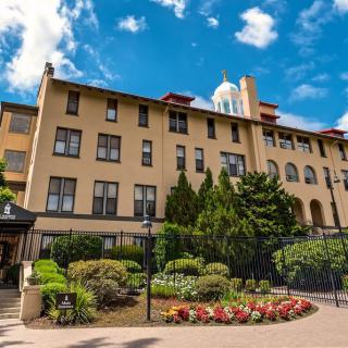 A beautiful hotel building surrounded by well-maintained gardens under a partly cloudy sky.