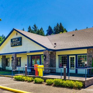 A restaurant with a buffet sign, featuring a spacious parking lot and clear blue skies.